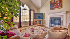 A living room with a fireplace, a large window with curtains, a television, and a painting on the wall.