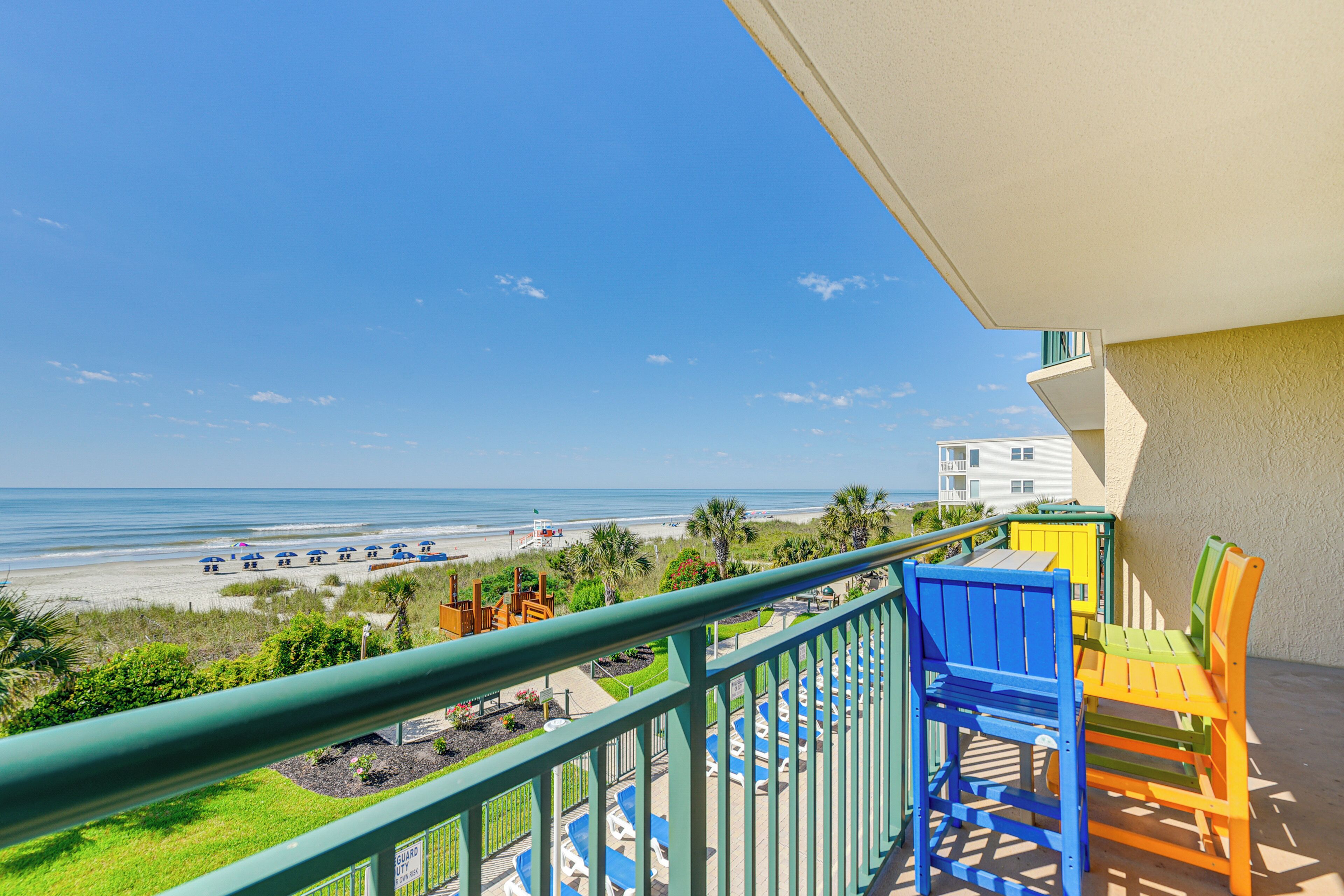 A balcony with colorful chairs and a view of the beach and ocean.