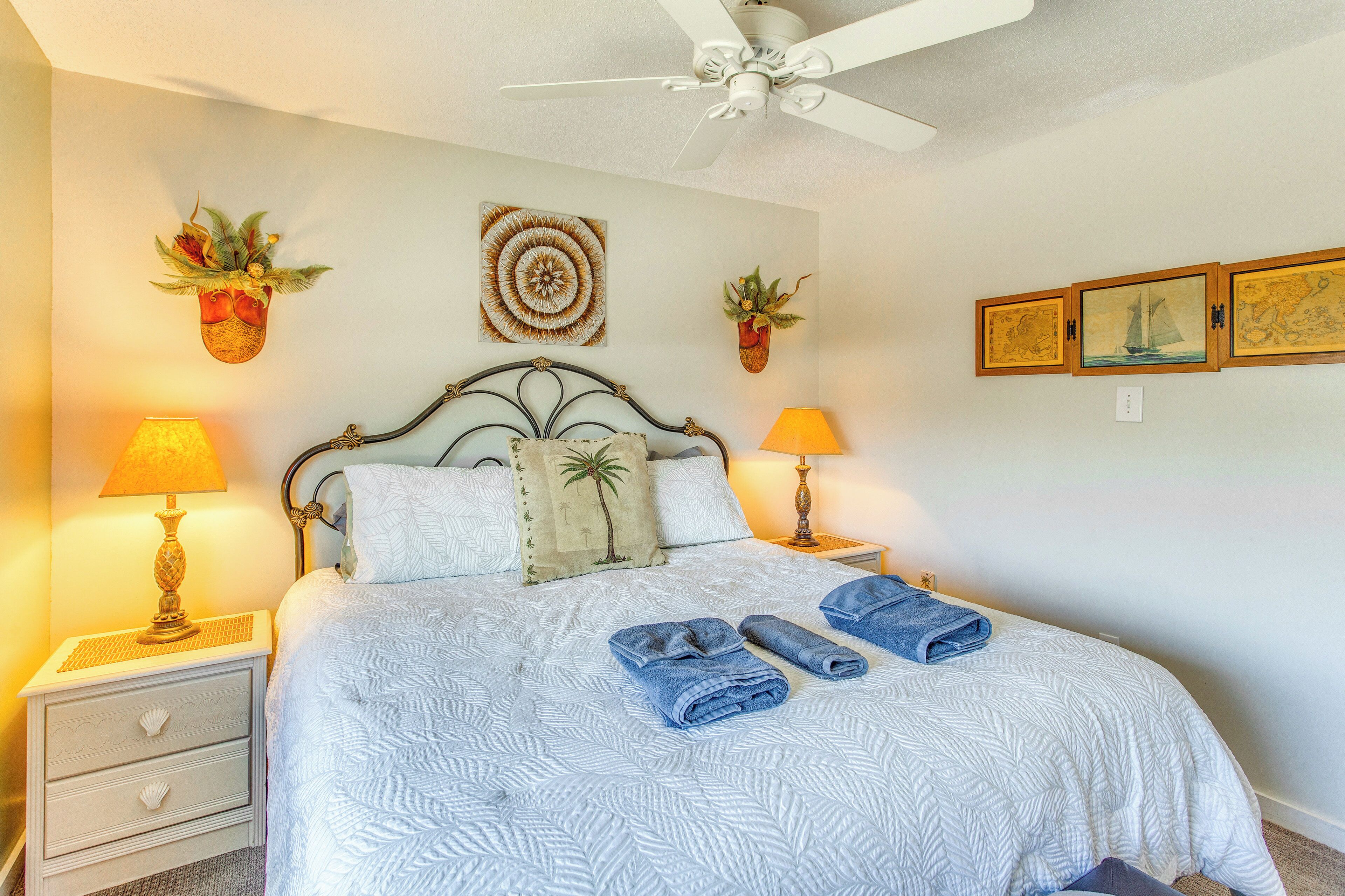 A neatly made bed with white bedding and blue towels, a ceiling fan, and wall-mounted lamps.