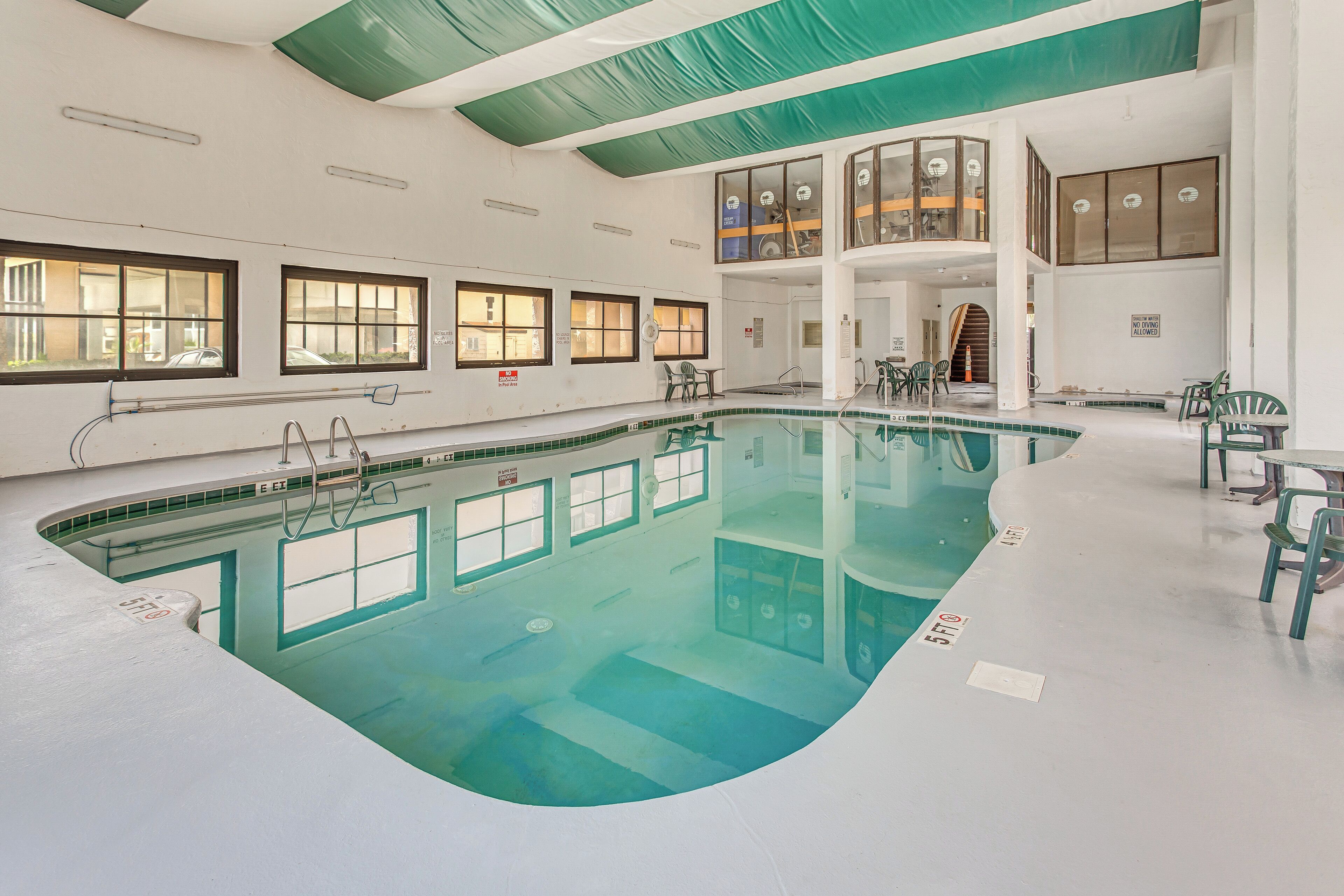 Une piscine intérieure à l’eau claire, dotée de nombreuses fenêtres et construite sur deux niveaux, avec un balcon.