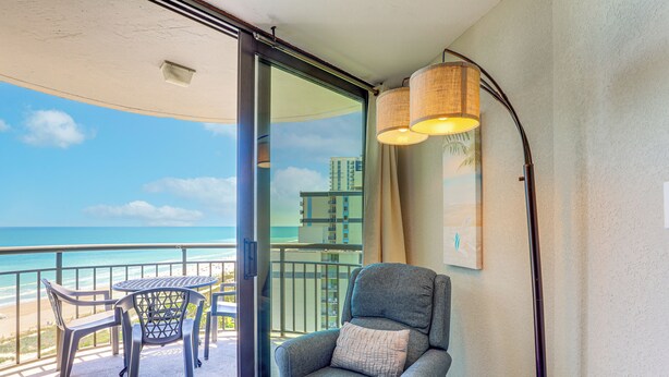 A balcony with a view of the beach, a chair, a small table, and a lamp. - Walk to Shore: Condo w/ 2 Pools in Myrtle Beach (Myrtle Beach)