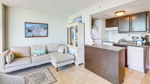 A living room with a sofa, a cabinet, and a kitchen area with a stove and sink. - Walk to Shore: Condo w/ 2 Pools in Myrtle Beach (Myrtle Beach)