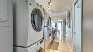 A laundry room with stacked washers and dryers, a tiled floor, and a hallway leading to other rooms. - Ocean-view Penthouse Condo in North Myrtle Beach! (North Myrtle Beach)