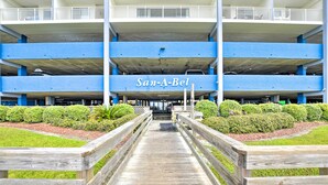 A multi-level parking garage with a wooden walkway leading to the entrance. - Ocean-view Penthouse Condo in North Myrtle Beach! (North Myrtle Beach)
