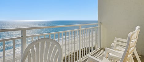 A balcony with white chairs overlooking a beach.