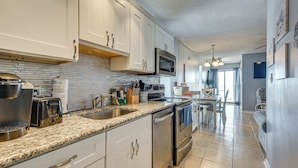 A modern kitchen with white cabinets, a granite countertop, stainless steel appliances, and a dining area with a table and chairs. - Ocean-view Penthouse Condo in North Myrtle Beach! (North Myrtle Beach)