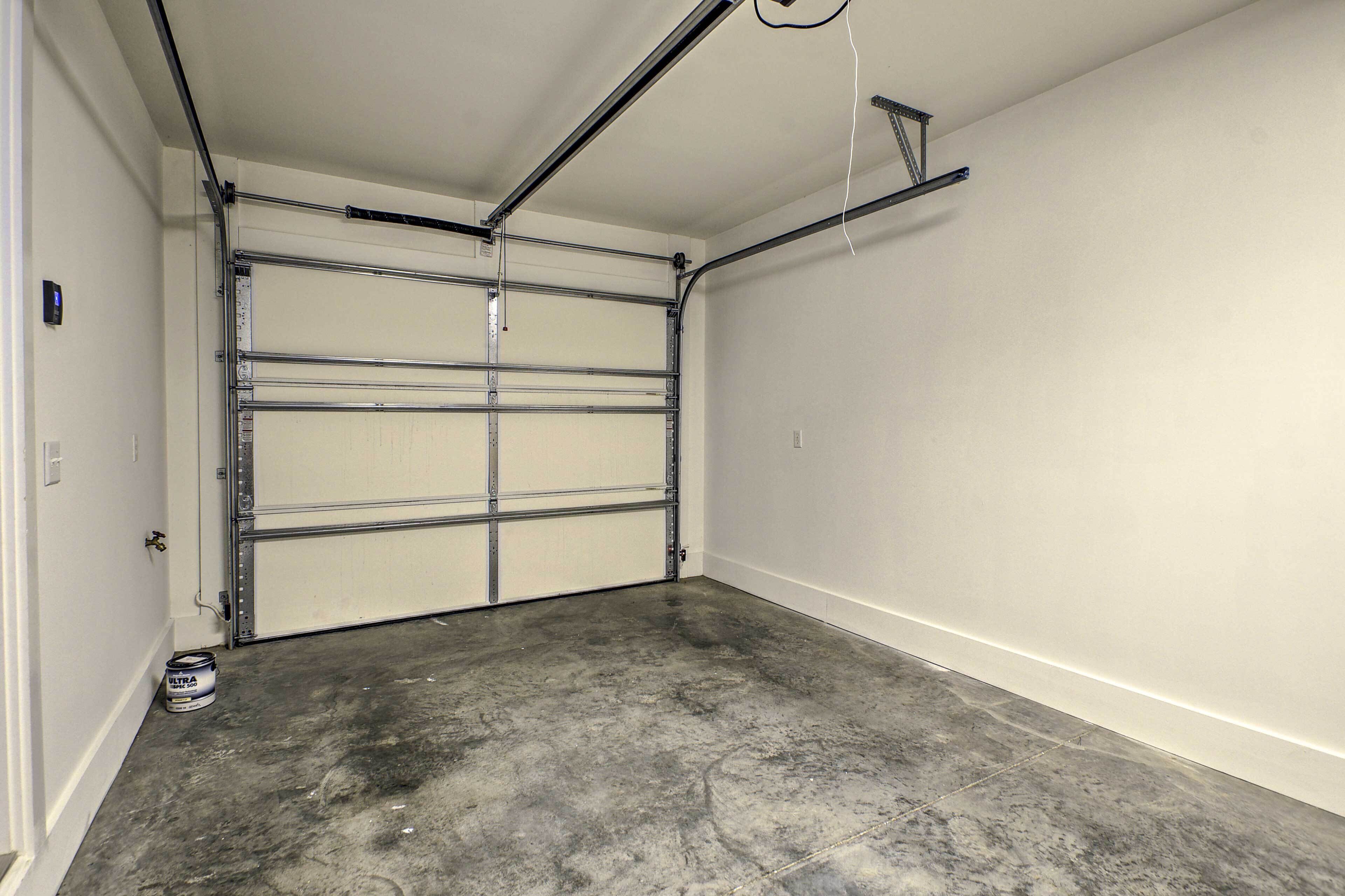 A garage with a concrete floor, a white door, and a metal garage door opener.