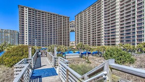 A multi-story hotel with balconies, a pool area, and a wooden boardwalk leading to the entrance. - Resort Perks & Pools: Townhome By Barefoot Landing (Myrtle Beach)