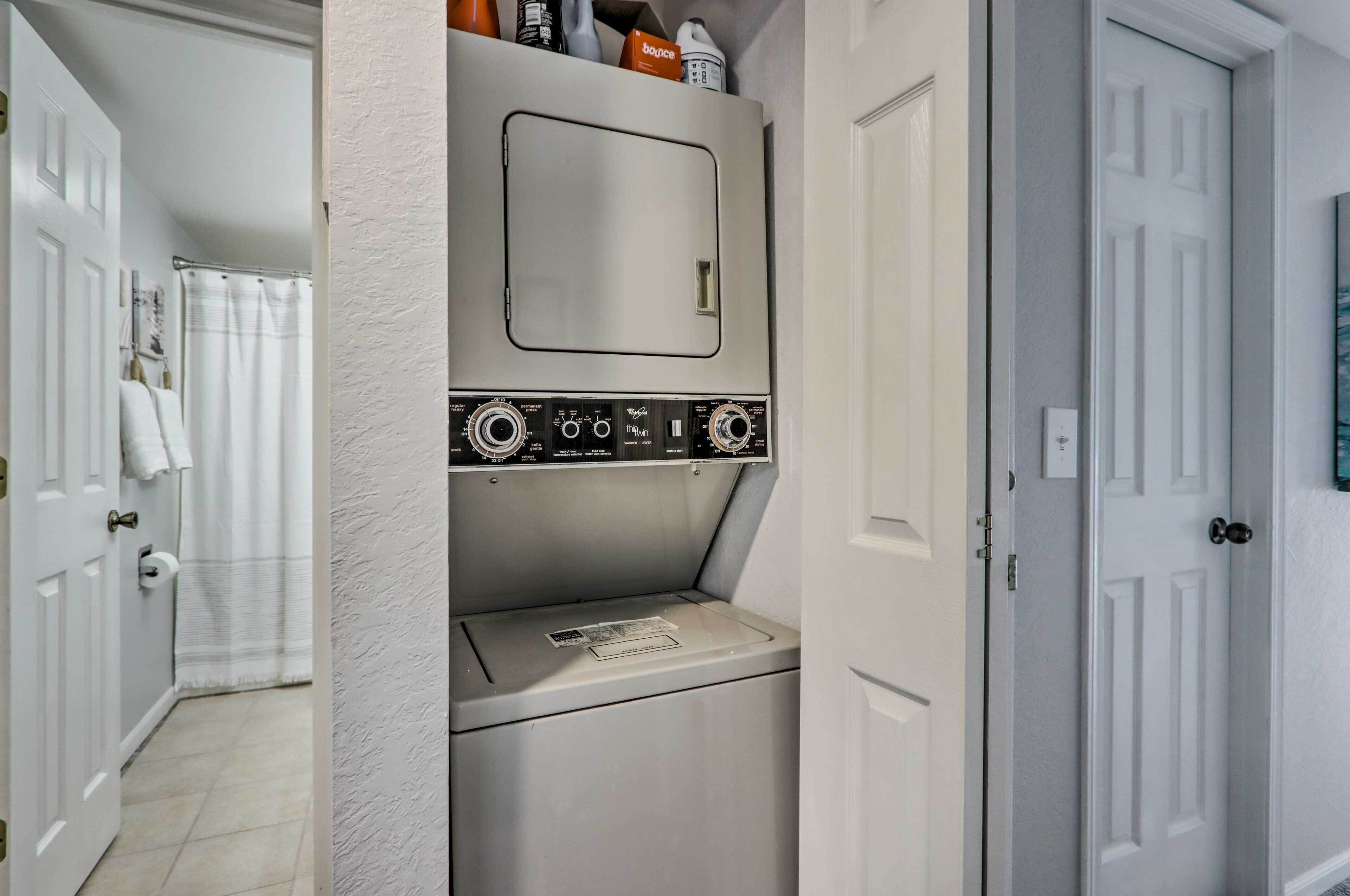 A compact laundry room with a washing machine and dryer, a small mirror, and a shelf with toiletries.
