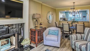 A living room with a fireplace, a dining area with chairs, and a kitchen in the background. - Myrtle Beach Vacation Rental w/ 2 Resort Pools! (Myrtle Beach)
