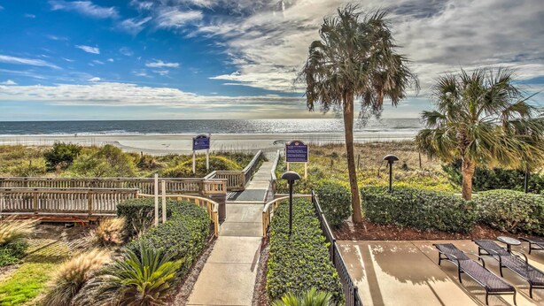 A beachfront walkway leading to a beach with palm trees and a wooden fence. - Myrtle Beach Vacation Rental w/ 2 Resort Pools! (Myrtle Beach)
