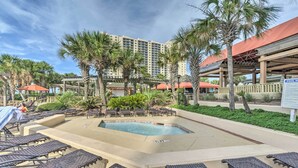 A pool area with lounge chairs, palm trees, and a building in the background. - Myrtle Beach Vacation Rental w/ 2 Resort Pools! (Myrtle Beach)