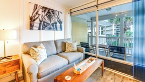 A modern living room with a sofa, a coffee table, and a large window offering a view of the outdoors. - Walkable Studio in North Myrtle Beach! (North Myrtle Beach)