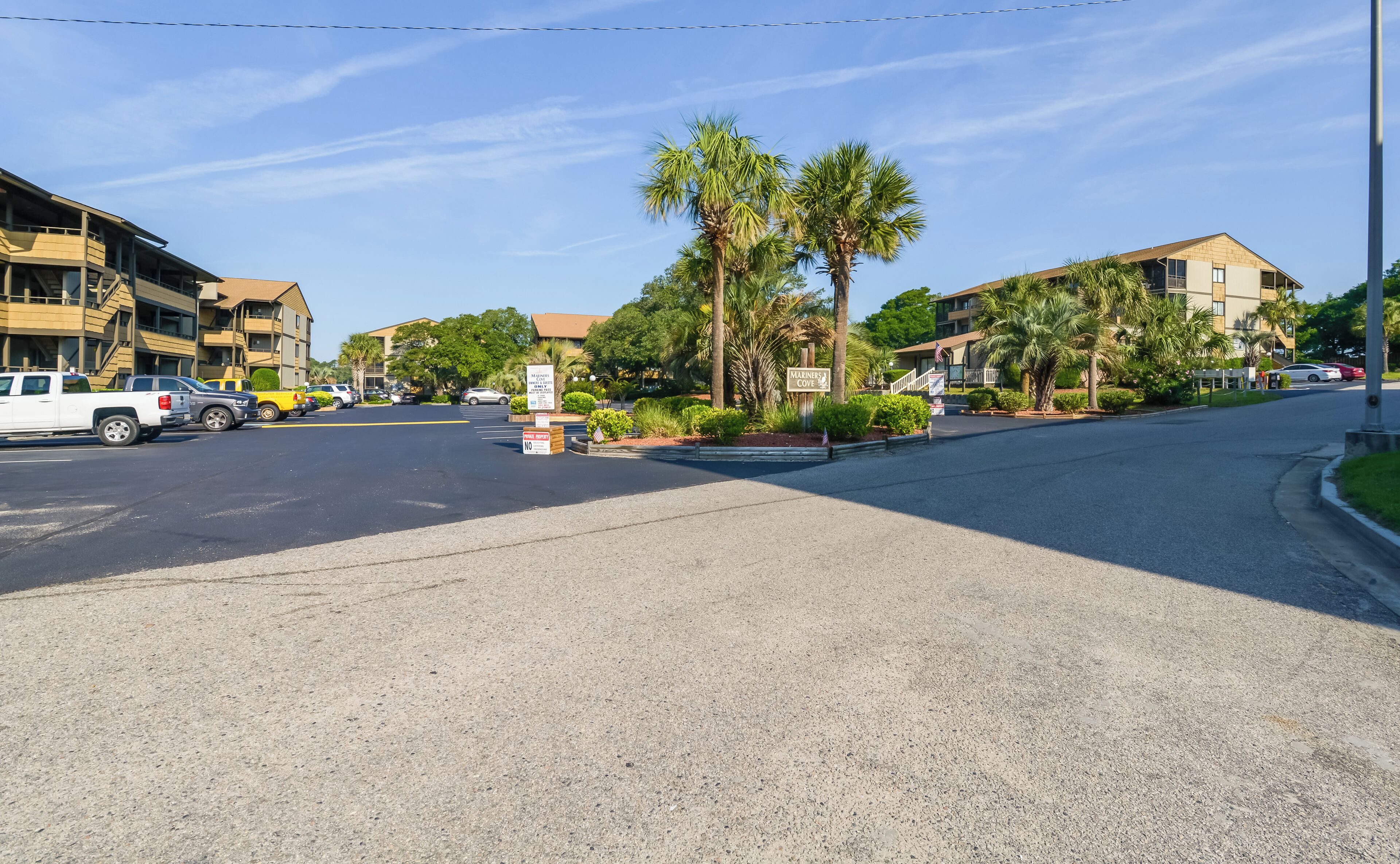 A street view with parked cars, palm trees, and buildings.