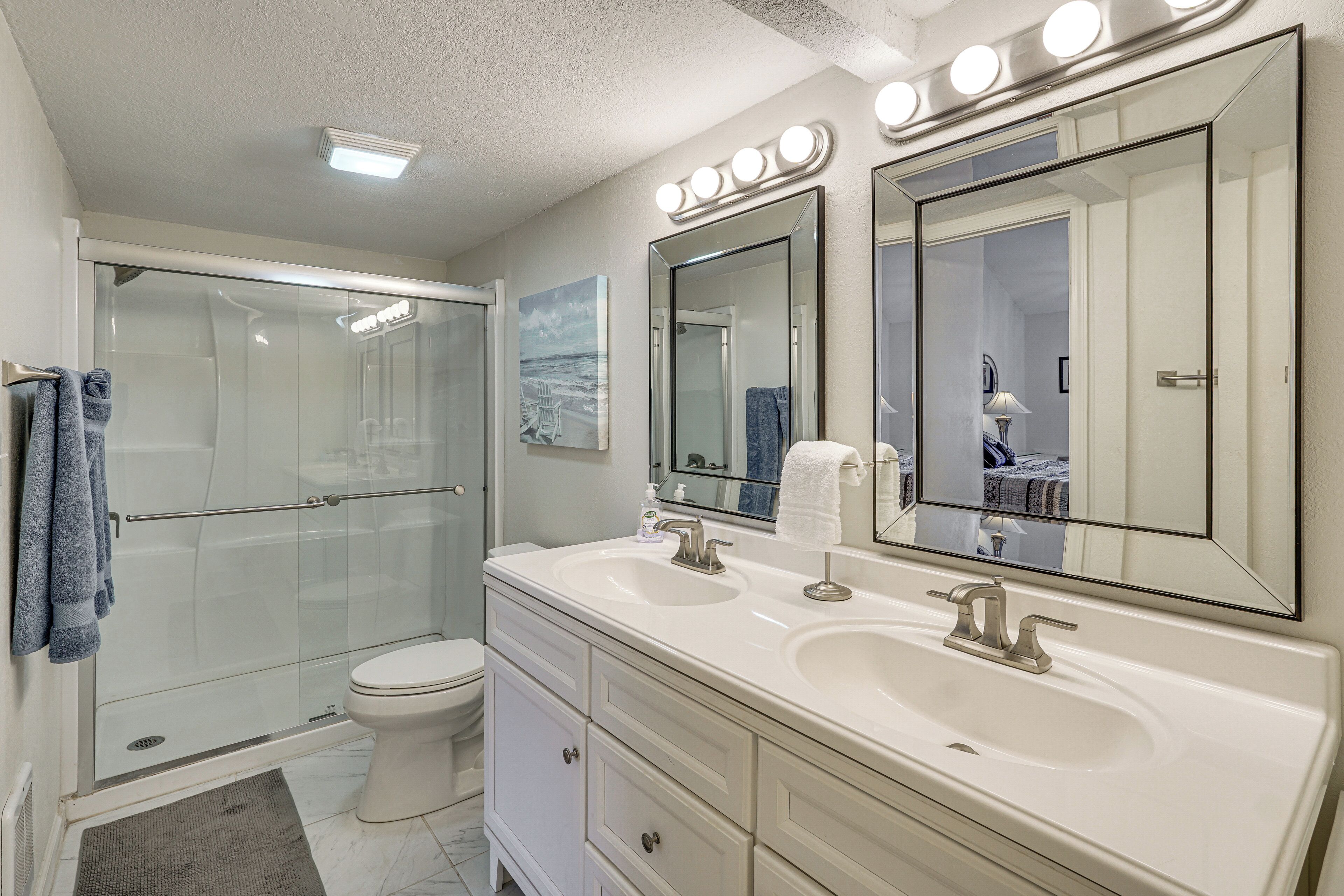 A modern bathroom with a glass shower enclosure, a toilet, a vanity with two sinks, and large mirrors.