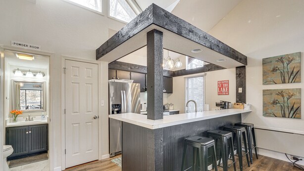 A modern kitchen with a central island, bar stools, a refrigerator, and a sign that reads "Powder Room". - Osage Beach Getaway - 1 Mi to Margaritaville Fun! (Osage Beach)