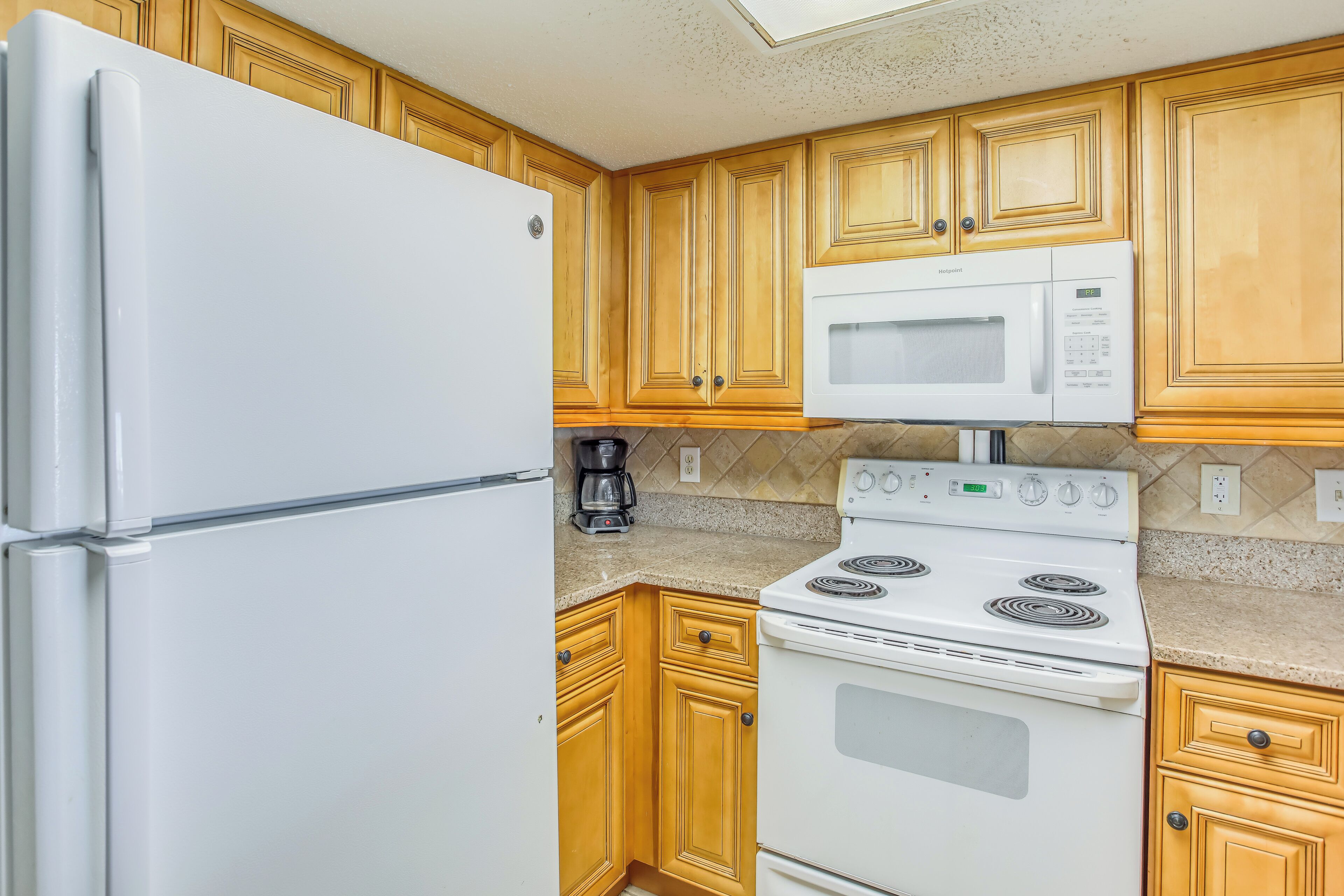 A kitchen with wooden cabinets, a white refrigerator, a microwave, and a stove.