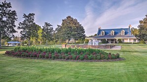 A large, stately building with a blue roof and white trim, surrounded by well-manicured lawns and a variety of flowering plants. - Pawleys Island Condo at True Blue Golf Resort (Pawleys Island)