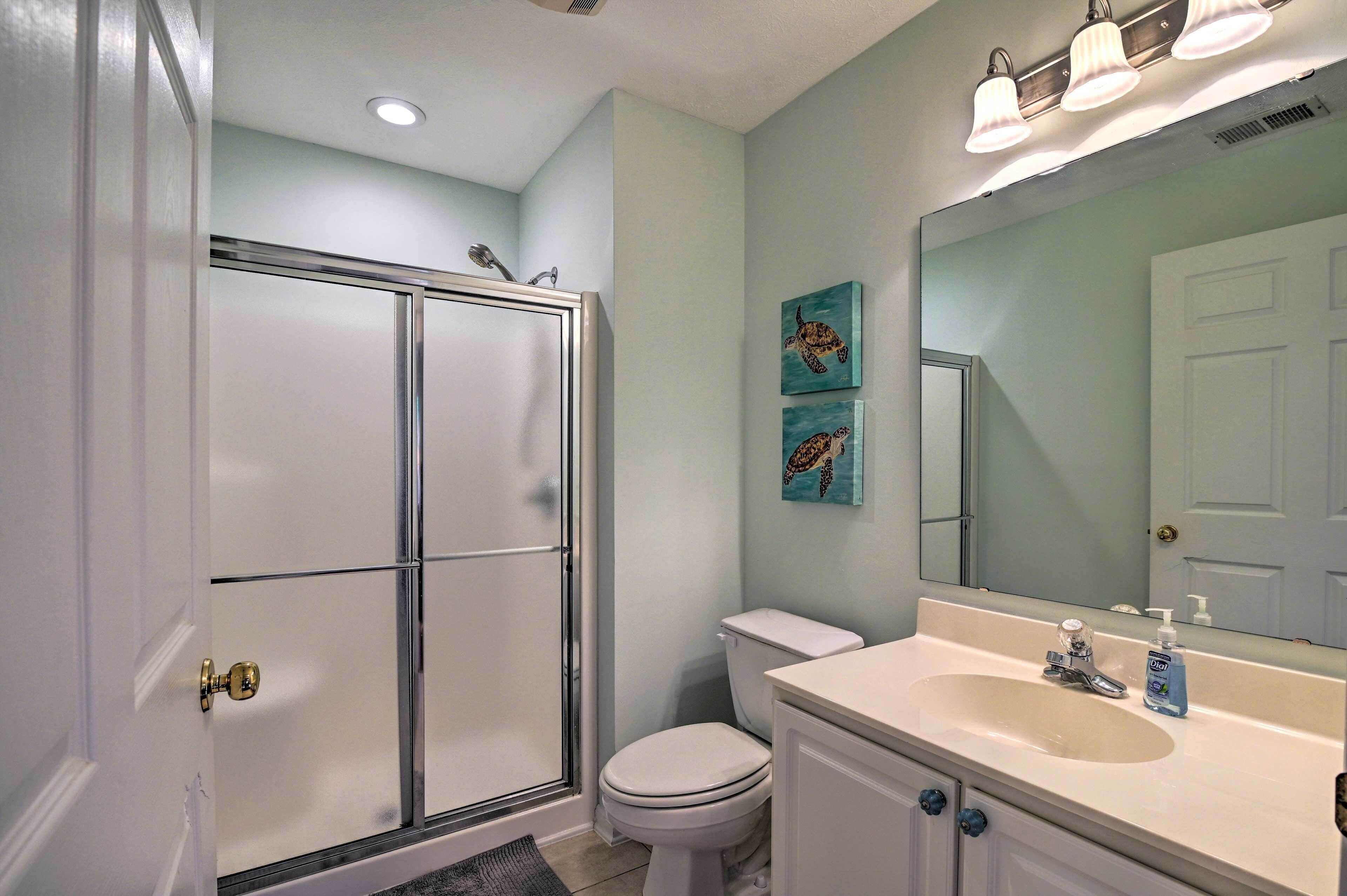 Une salle de bain avec une douche à parois de verre, des toilettes blanches, un lavabo avec un miroir et deux tableaux représentant des tortues, accrochés au mur.