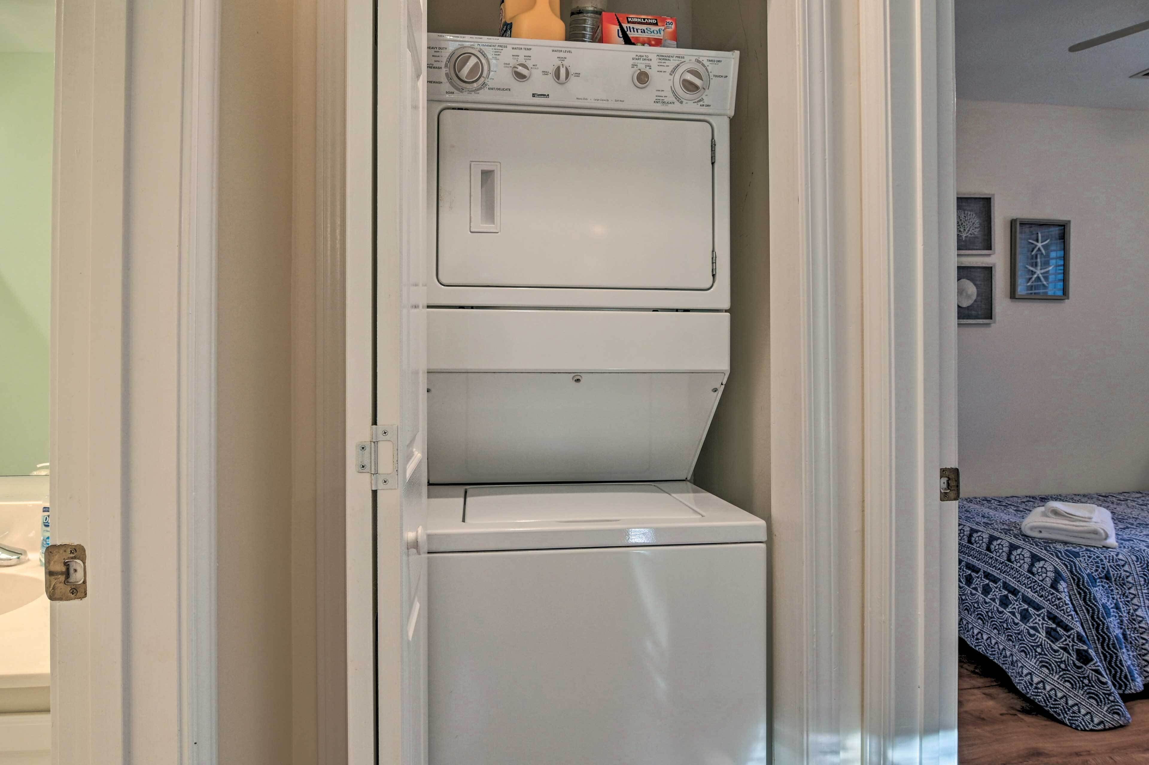 Een wasserette met gestapelde wasmachines en drogers, een bed met beddengoed met een patroon, en een muur met ingelijste foto's.