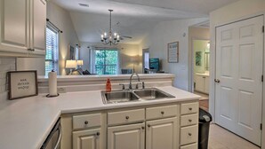 A kitchen with a double sink, white cabinets, a chandelier, and a framed sign on the counter. - Pawleys Island Condo at True Blue Golf Resort (Pawleys Island)