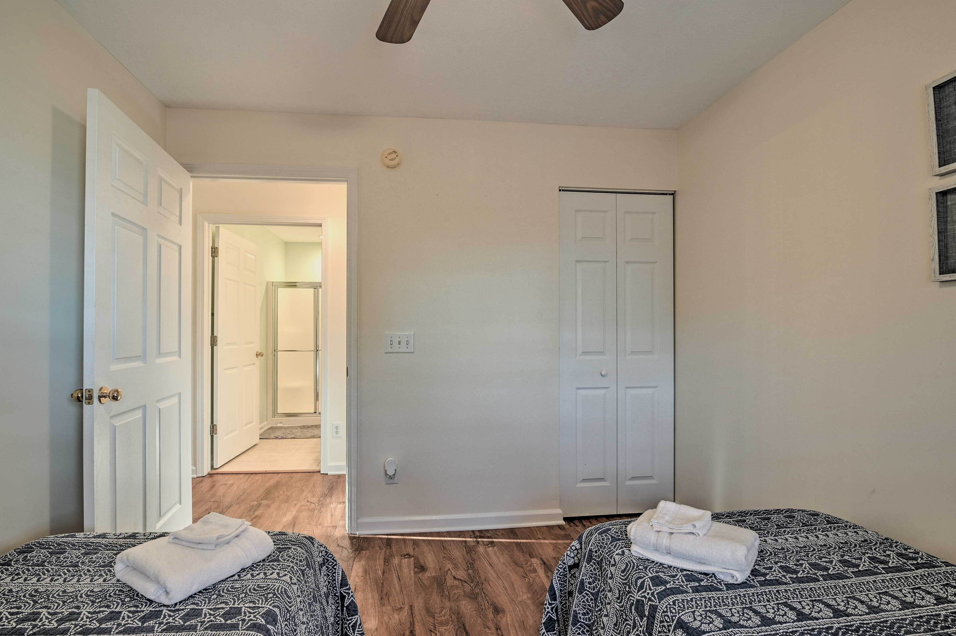 A hotel room with two beds, a door leading to a bathroom, and a ceiling fan.