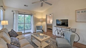 A living room with a sofa, armchair, coffee table, and a ceiling fan. There is a television and a bicycle with a basket. - Pawleys Island Condo at True Blue Golf Resort (Pawleys Island)