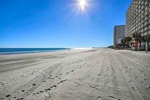 A beach with a clear sky and a sun shining. There are footprints in the sand and a building on the right. - Oceanfront Vacation Rental in Murrells Inlet! (Murrells Inlet)