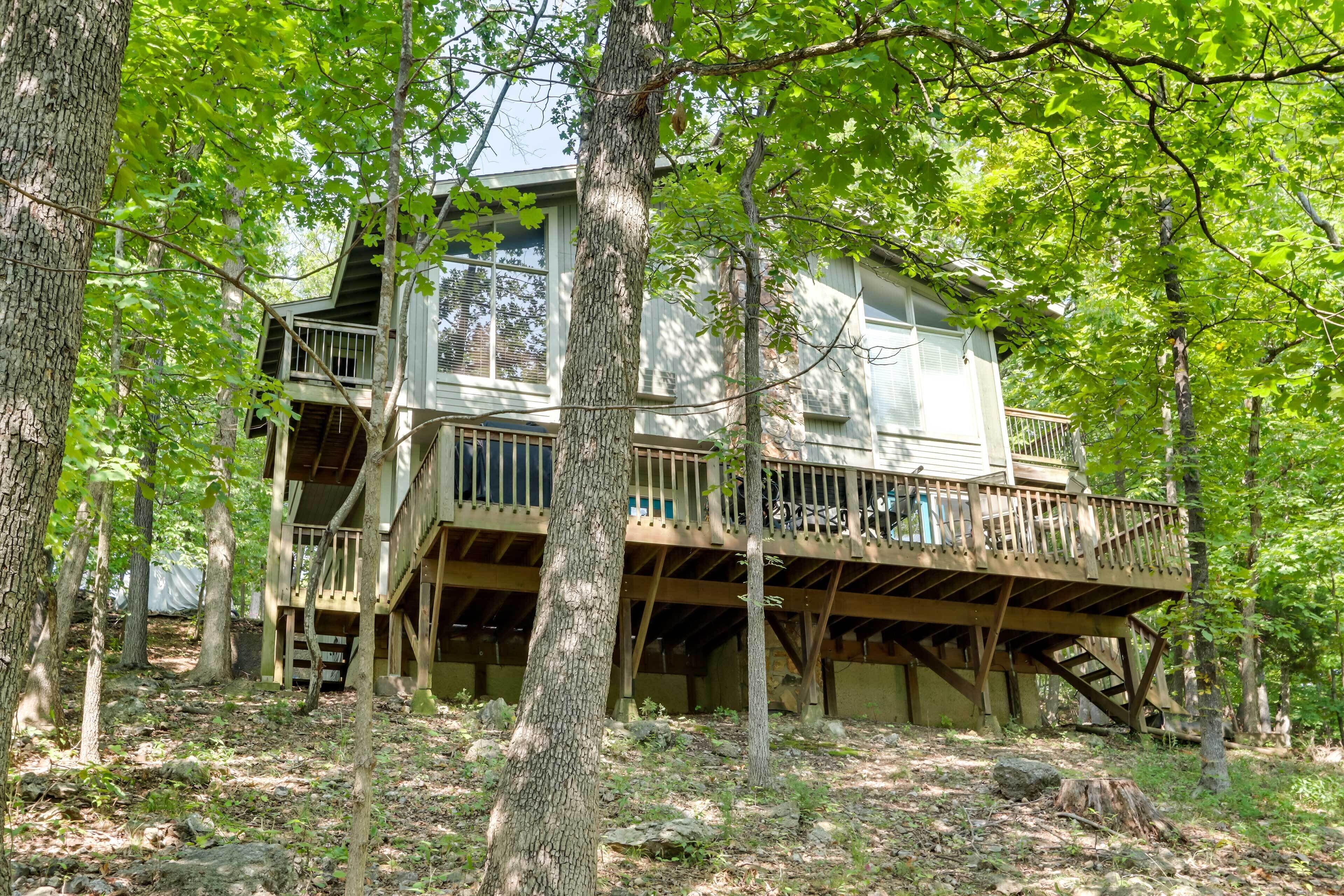 Une cabane dotée d’une terrasse en bois et de plusieurs niveaux, entourée d’arbres.