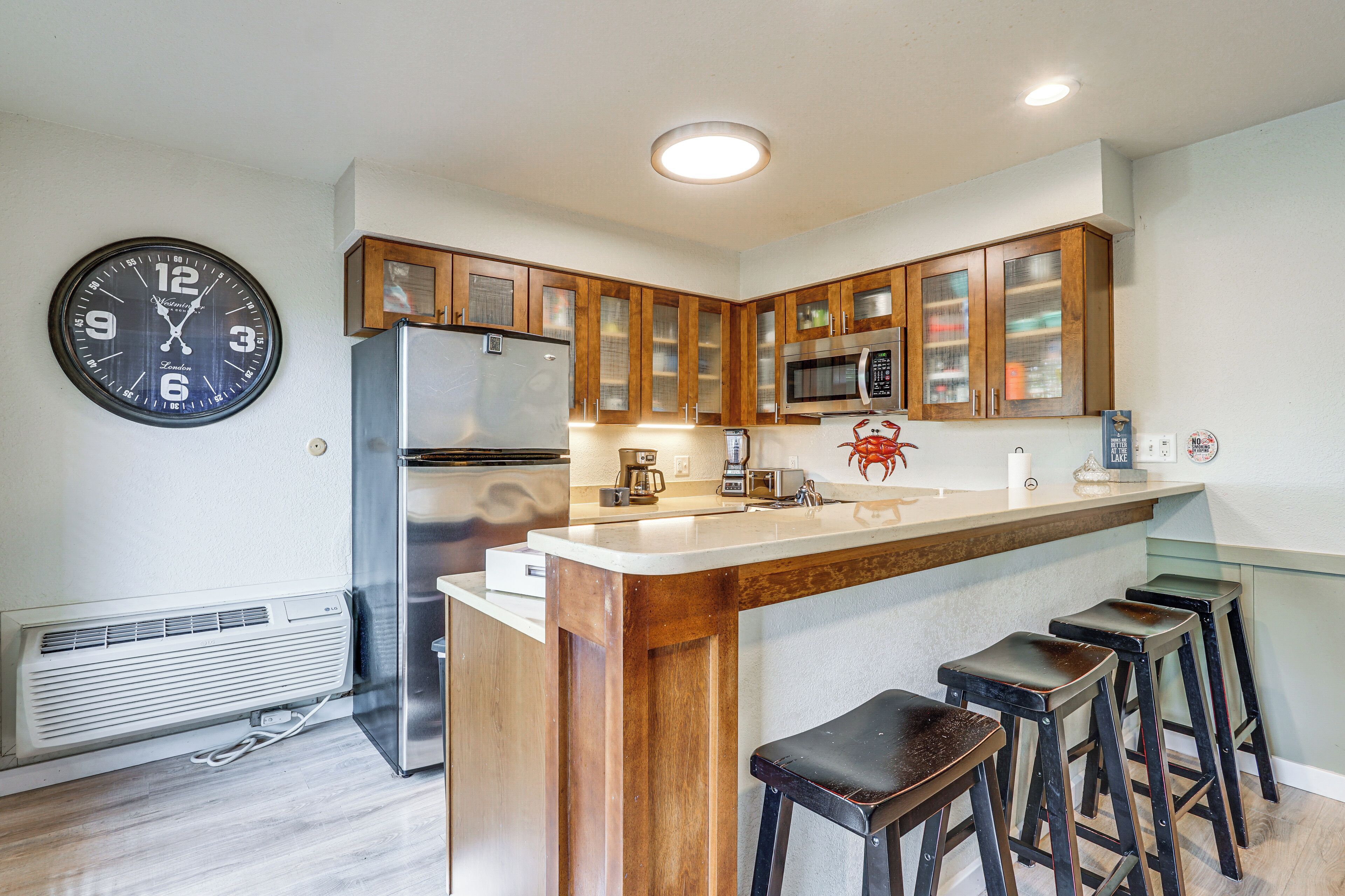 A modern kitchen with wooden cabinets, a stainless steel refrigerator, a microwave, and a large wall clock.