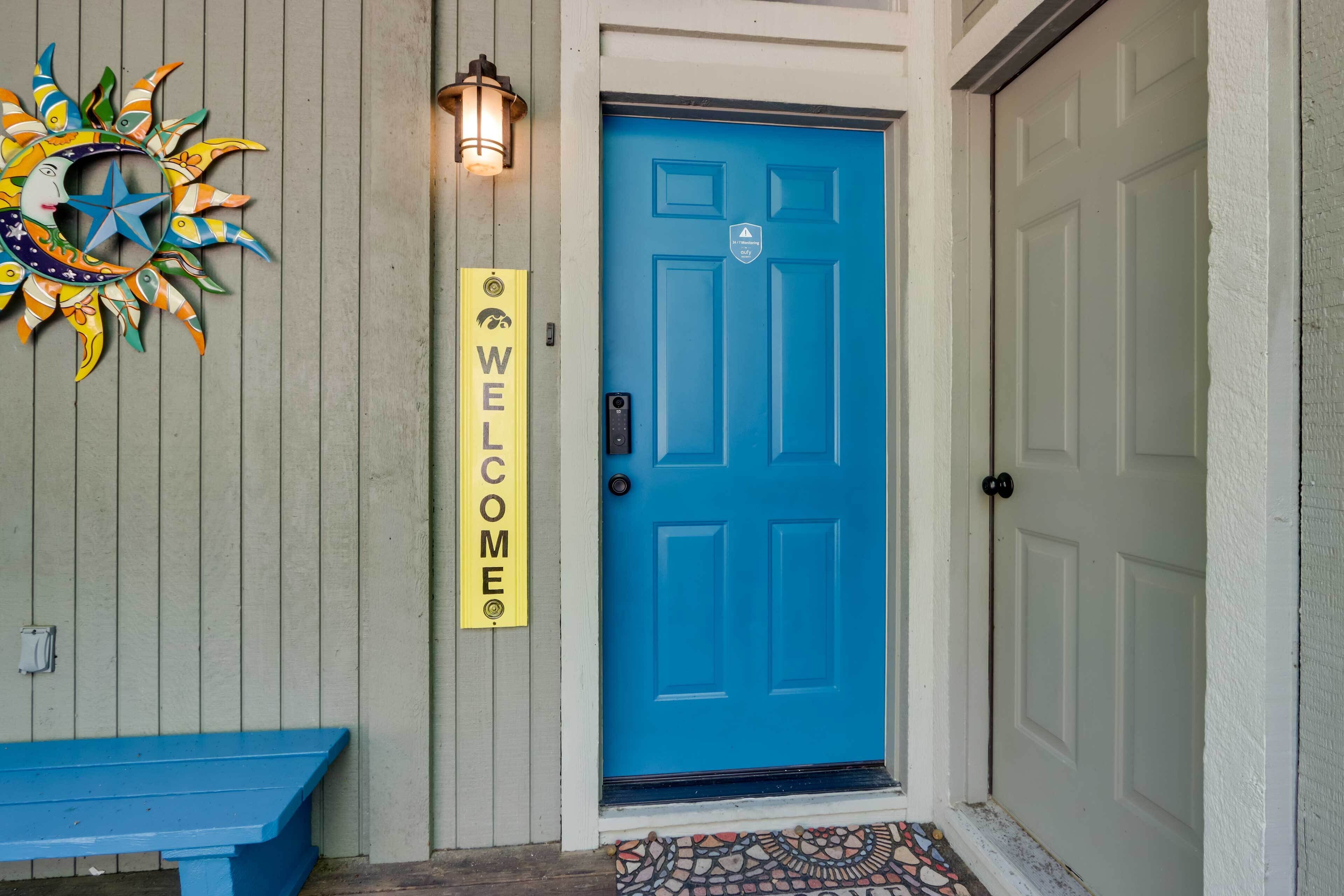 A blue door with a welcome sign, a colorful sun decoration, and a bench outside.