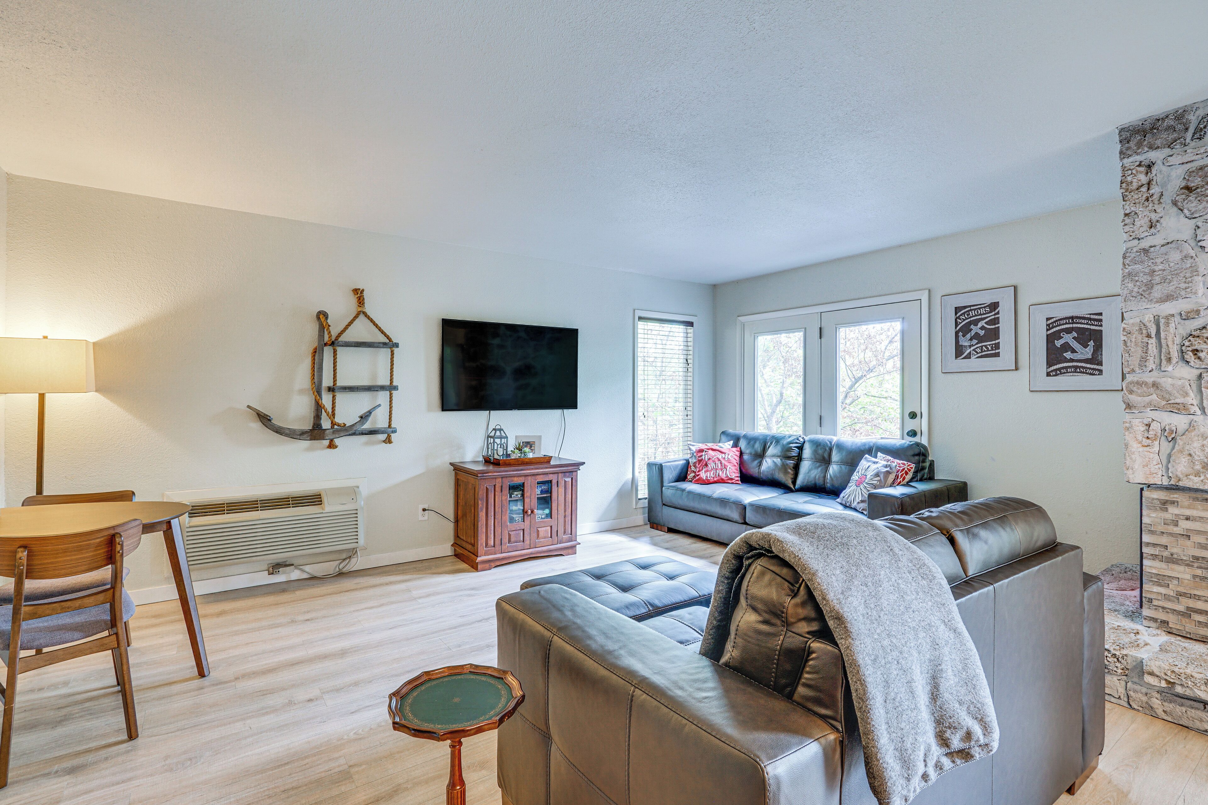 Een woonkamer met een leren bank, een houten tafel, een aan de muur bevestigde televisie en een open haard met stenen muren.