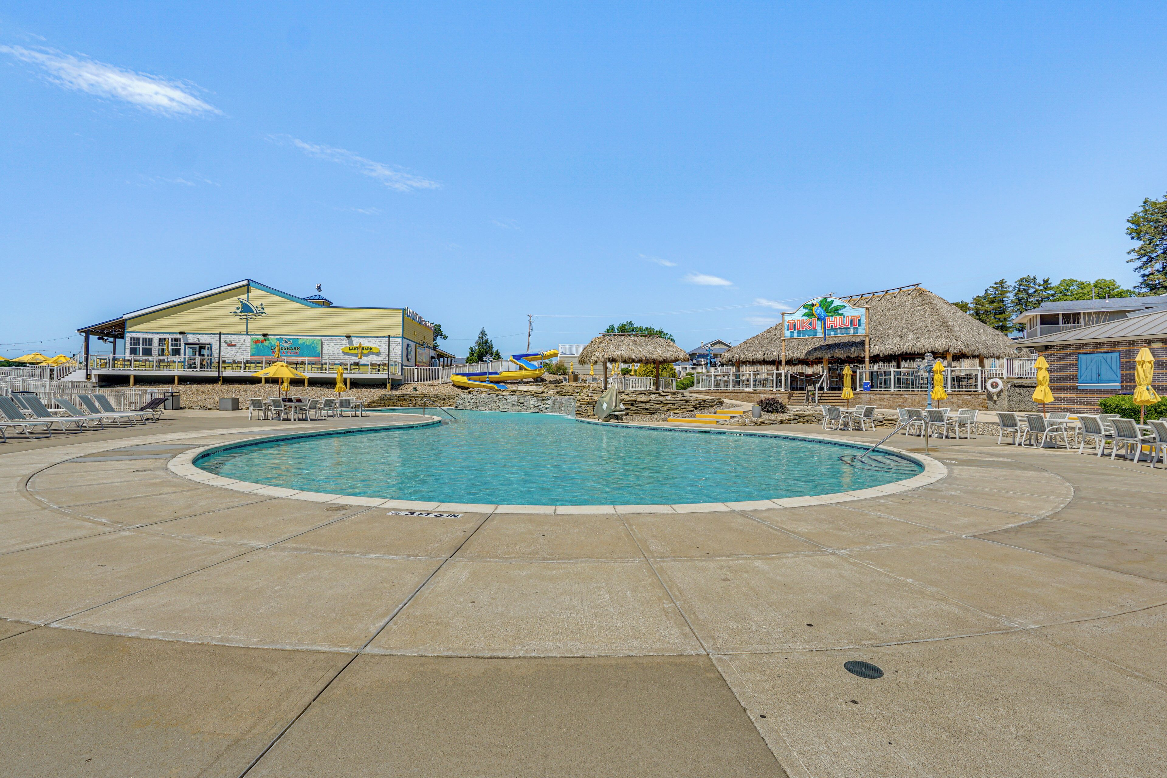 A swimming pool with lounge chairs and umbrellas, surrounded by buildings with signs.