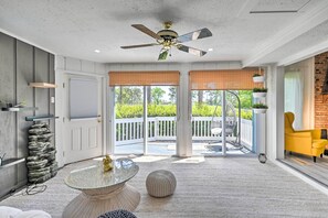 A spacious room with a ceiling fan, a glass table, a round ottoman, and a yellow chair.