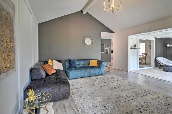 A modern living room with a dark grey couch, a glass coffee table, and a patterned rug.