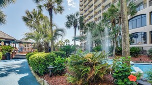 A hotel courtyard with a swimming pool, palm trees, and a fountain. - Oceanfront Condo w/ Views in North Myrtle Beach! (North Myrtle Beach)