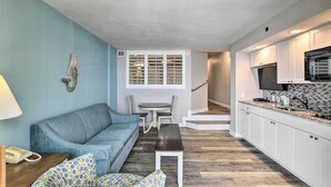A compact living space with a blue sofa, a small dining table, a bench, and a kitchen area with white cabinets and a black microwave. - Oceanfront Condo w/ Views in North Myrtle Beach! (North Myrtle Beach)