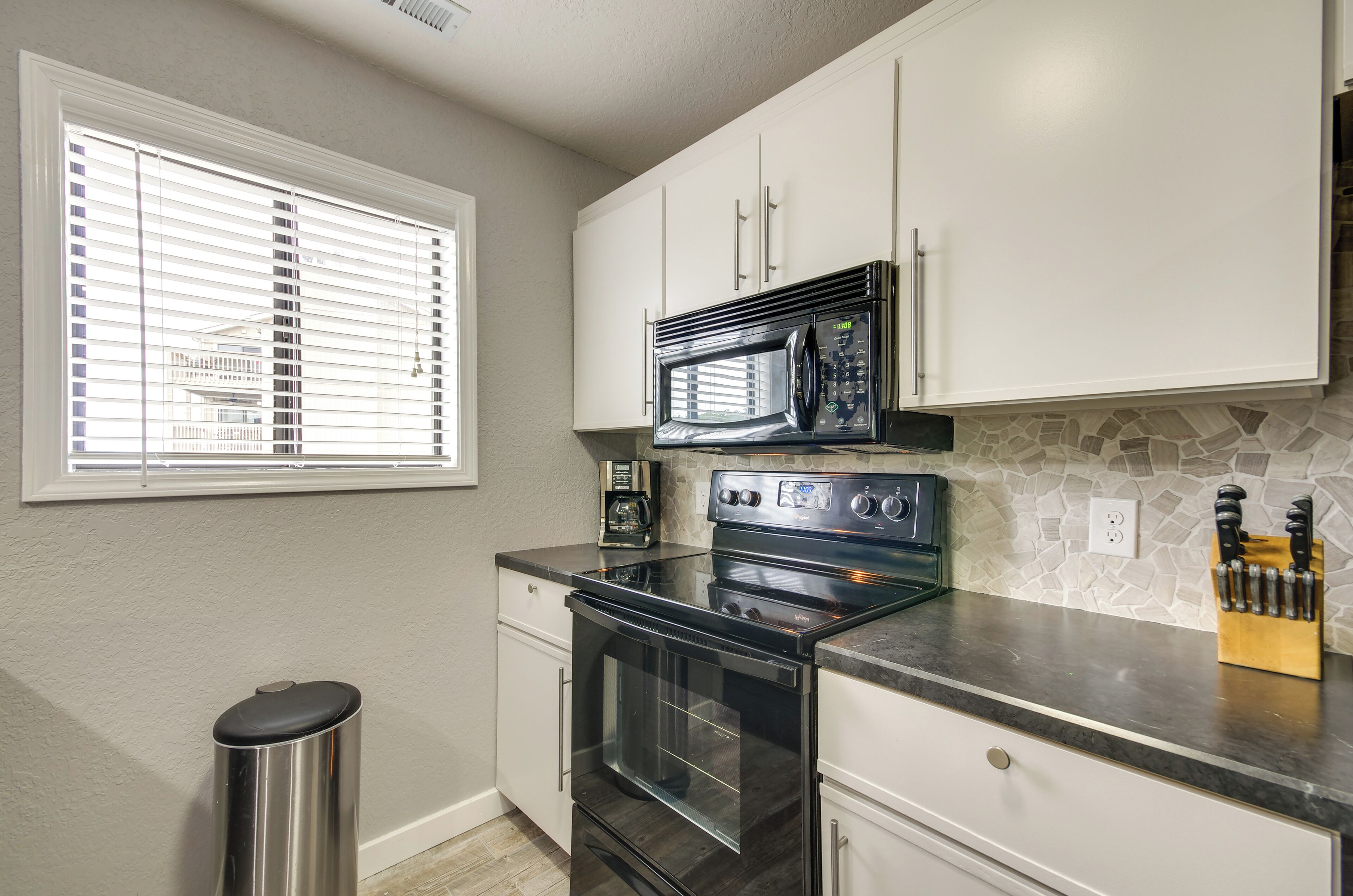 A kitchen with white cabinets, a black microwave, a stove, and a coffee maker.