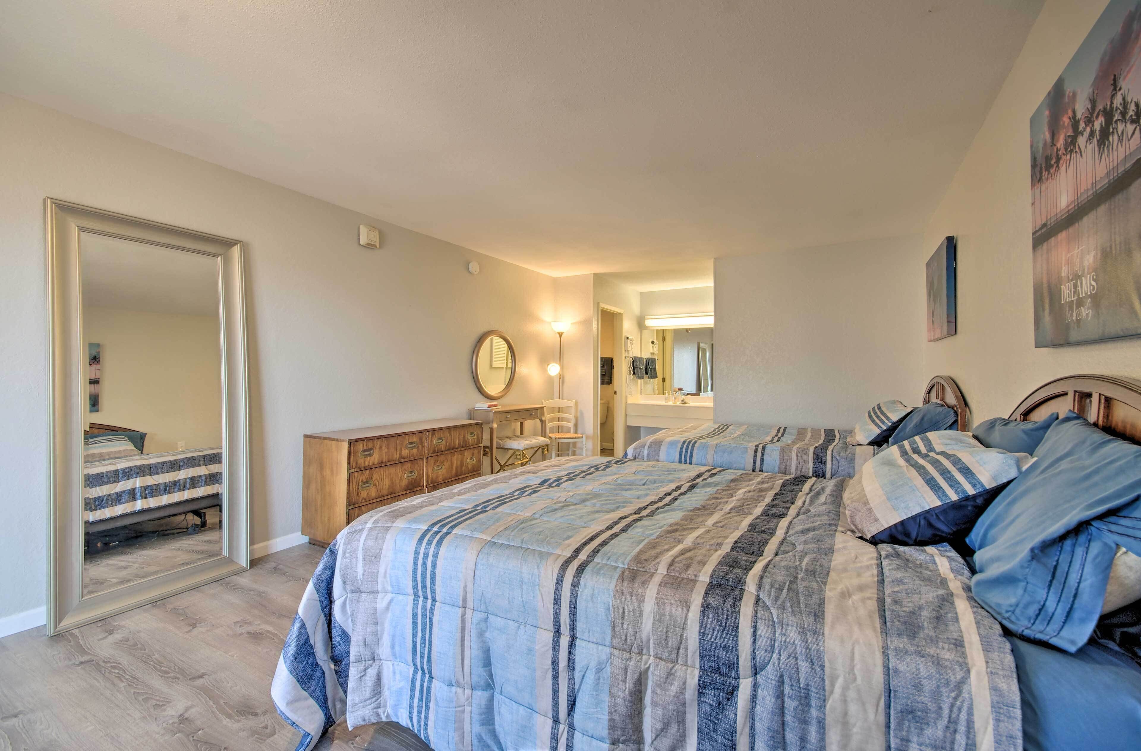 A bedroom with two beds, a dresser, a mirror, and a door leading to another room.