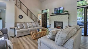 A spacious living room with a staircase, a fireplace, and a large window. - Dock, Slide + Fire Pit: Osage Beach Lake House (Osage Beach)