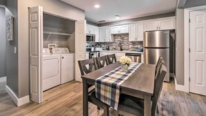 A modern kitchen with white cabinets, stainless steel appliances, and a dining area with a plaid tablecloth. - Pet-friendly Abode, Walk to Table Rock Lake! (Kimberling City)