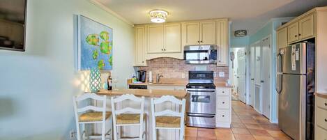 A kitchen with white cabinets, a brick backsplash, stainless steel appliances, and a wooden island with chairs.