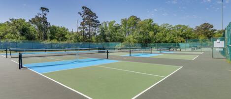 Canchas de tenis múltiples, rodeadas por una valla verde y árboles.