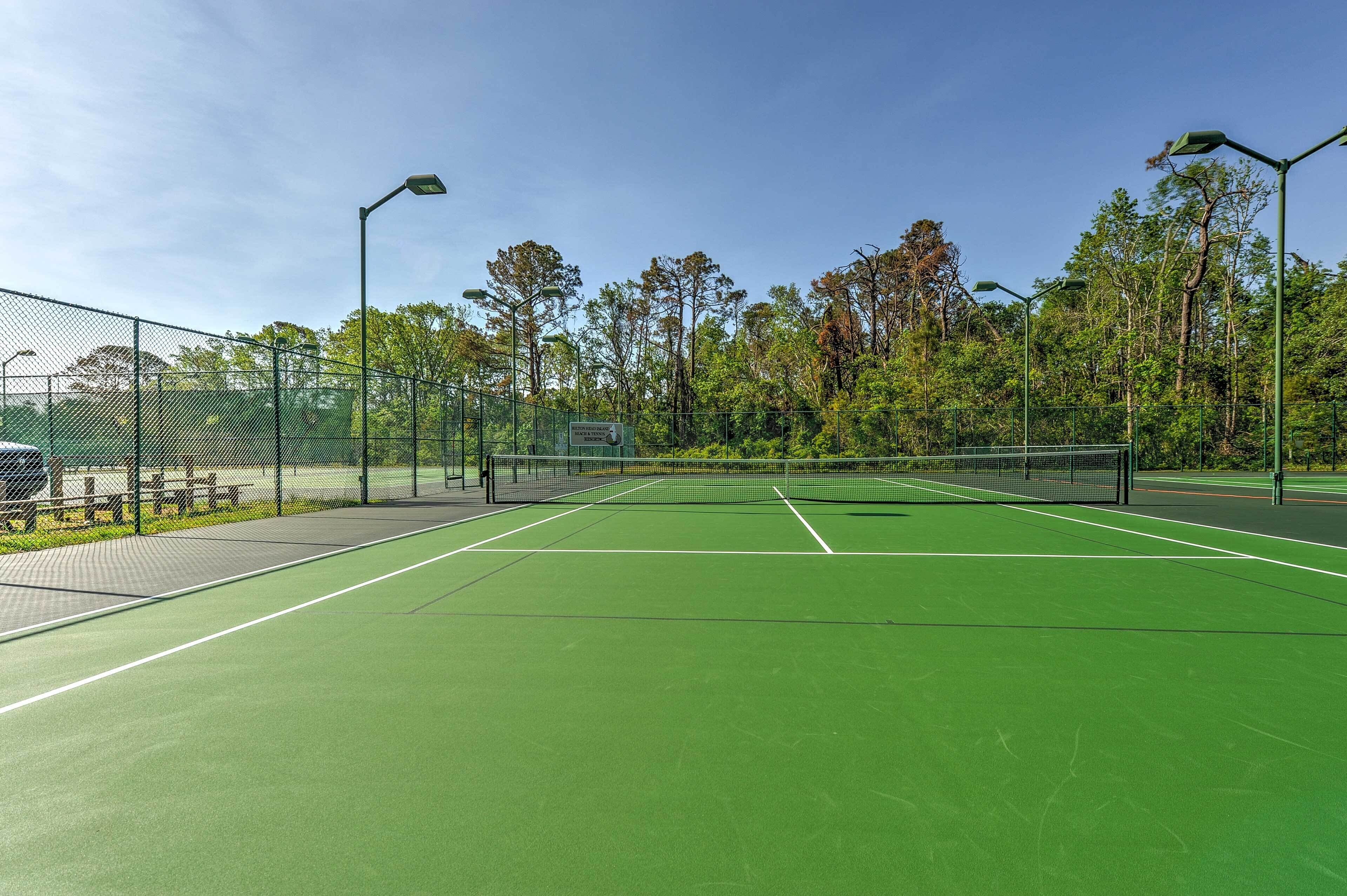 Ulkotenniskenttä, jossa on verkko, ja jonka ympärillä on aita ja puita.