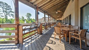 Eine Terrasse im Freien mit Holztischen und -stühlen, einem Holzgeländer und Blick auf Wasser und Bäume.