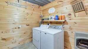 Une buanderie avec des murs en bois, un lave-linge, un sèche-linge et une étagère contenant des produits de nettoyage.