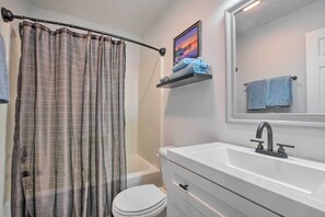 A bathroom with a striped shower curtain, a white sink with a modern faucet, a toilet, and a shelf with towels.
