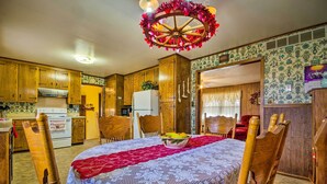A dining area with a table set for four, surrounded by wooden chairs, a chandelier, and a red table runner. - Peaceful Missouri Home, 25 Mi to Truman Lake! (Cole Camp)
