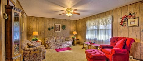 A living room with wooden paneling, a ceiling fan, a red armchair, a floral sofa, and a wooden cabinet.