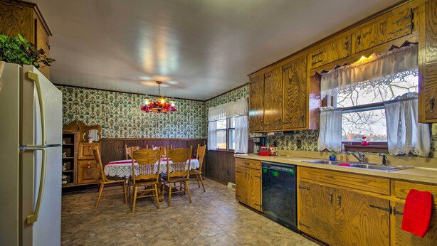 A kitchen with wooden cabinets, a dining table with chairs, a refrigerator, and a window with curtains.